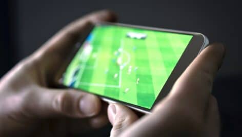 Sports tech concept: Watching football and sport stream with mobile phone. Man streaming soccer game live, video replay or highlights online with smart device. Sports fan and program of tv network in smartphone screen.