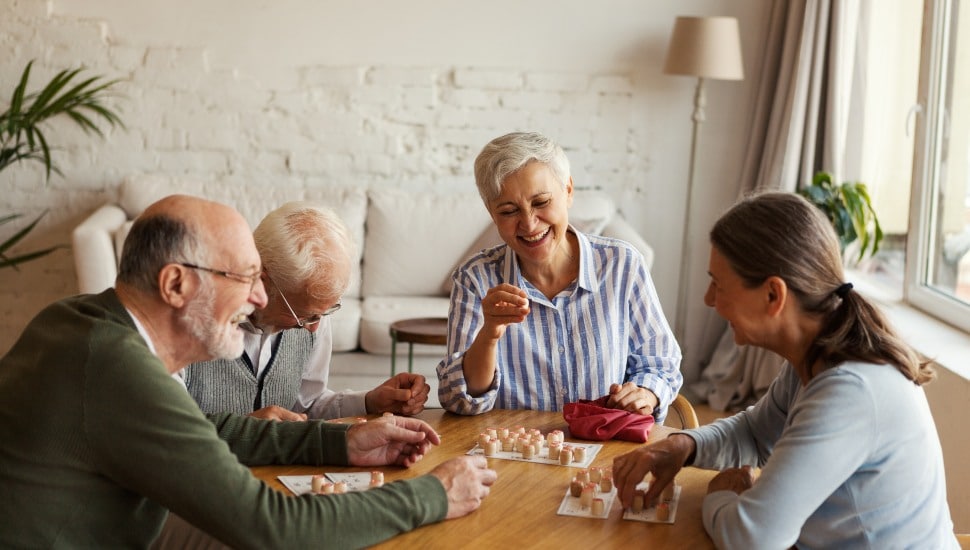 Group of four cheerful senior people, two men and two women, having fun sitting at table and playing bingo game.