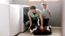 Father and daughter play with dog while doing laundry.