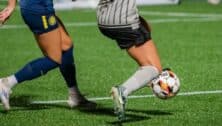 Two female soccer players fighting for possession of the ball.