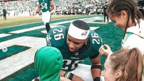 Saquon Barkley kneeling in the end zone to speak with two children.