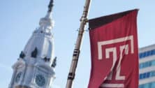 A Temple University flag waving in front of Philadelphia's City Hall.