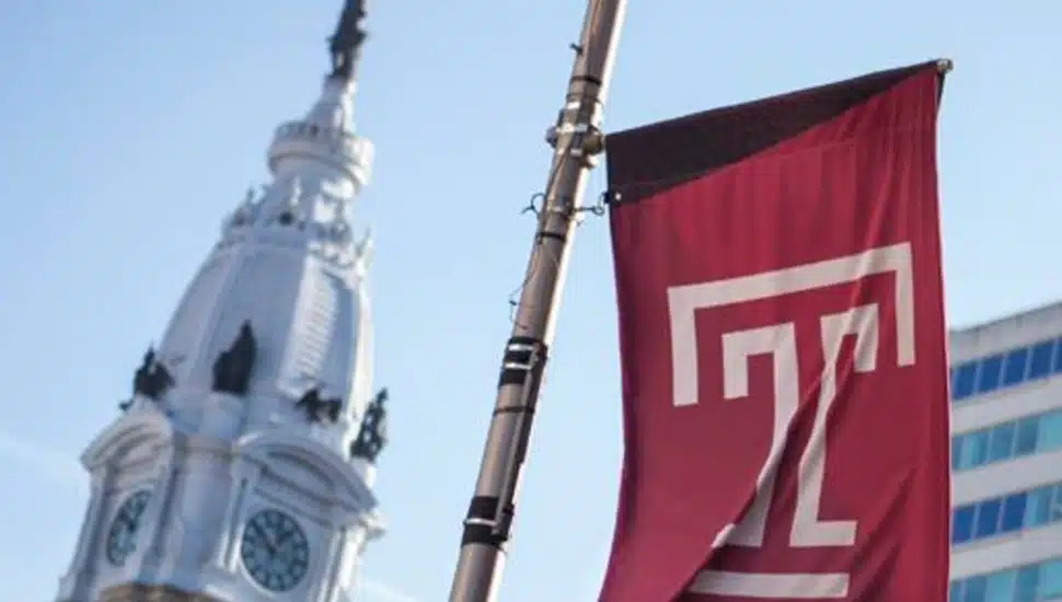 A Temple University flag waving in front of Philadelphia's City Hall.