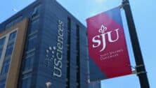 Outside the University of the Sciences building with an SJU flag in the forefront.