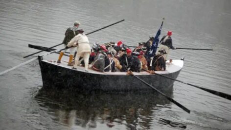 Actors reenacting the Washington Crossing in a boat on the water.