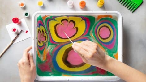 Close up of a woman marbling with paint on paper.