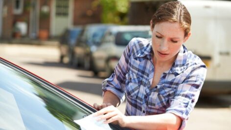 A distressed woman takes a parking ticket off of her windshield.