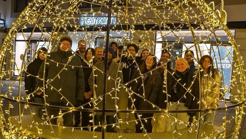 A group of PSU Abington students studying abroad posing behind an lit orb structure.