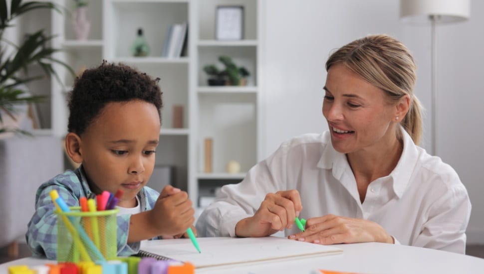 A staff professional works with a young boy as he draws.