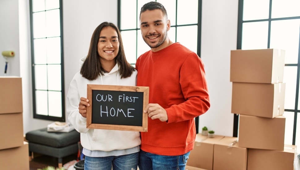 Young couple holding a sign that reads "OUR FIRST HOME."