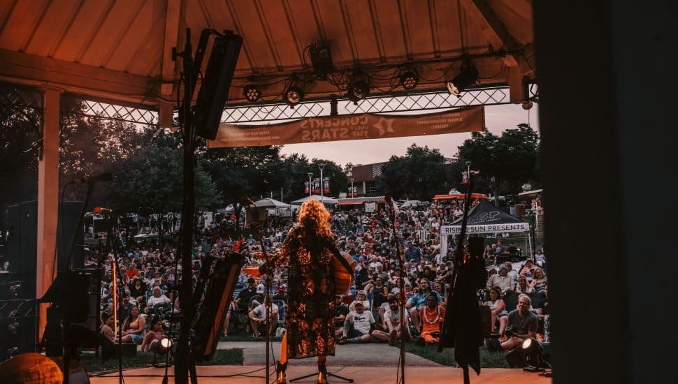 Musician performing at dusk for KOP's Concerts Under The Stars, surrounded by a full audience.