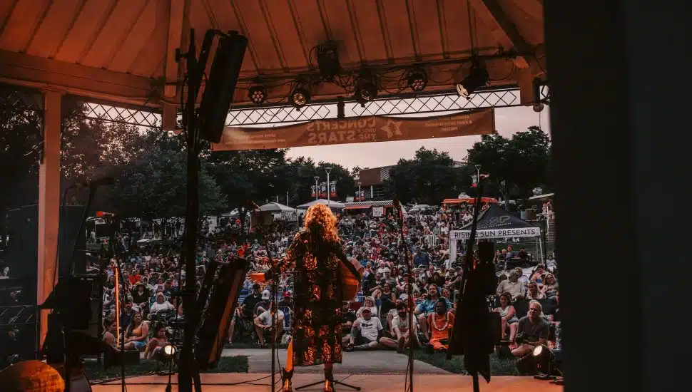Musician performing at dusk for KOP's Concerts Under The Stars, surrounded by a full audience.