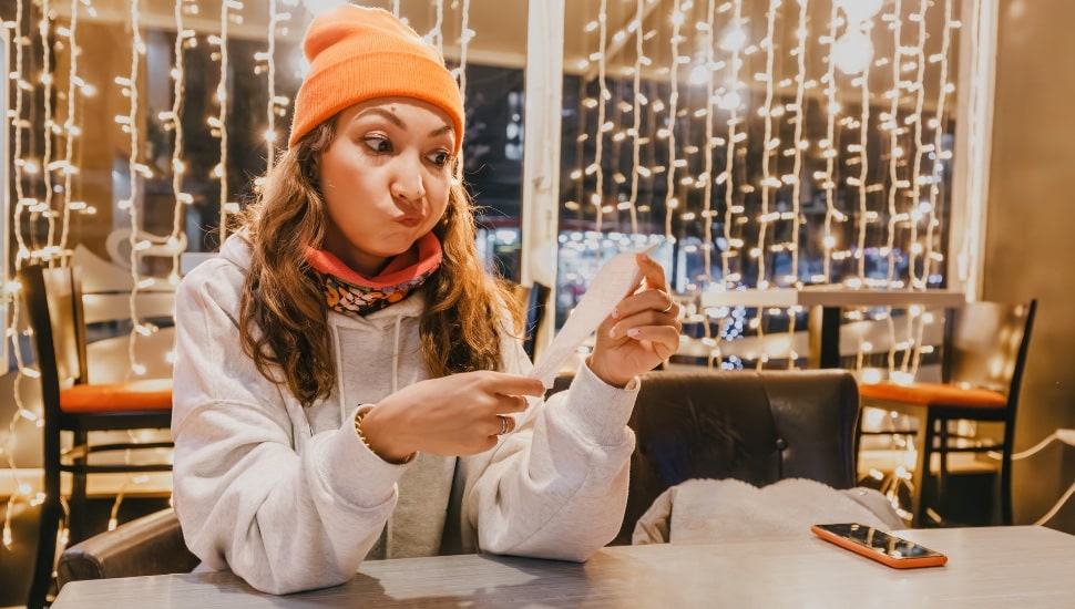 Startled woman scrutinizes the bill at the cafe, registering the crisis of emotion as she's shocked by the exorbitant price, realizing the hefty sum she must pay.