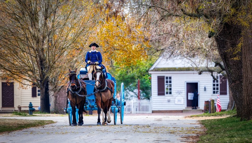 A man in Colonial garb on a horse-drawn carriage.