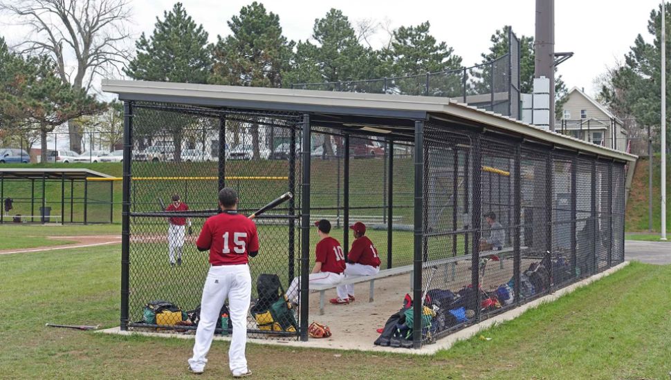 A small shelter provides cover for a dugout at a community baseball game.