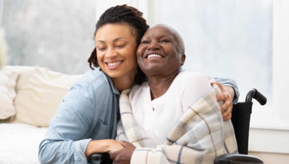 A woman hugs an older woman in a wheelchair.