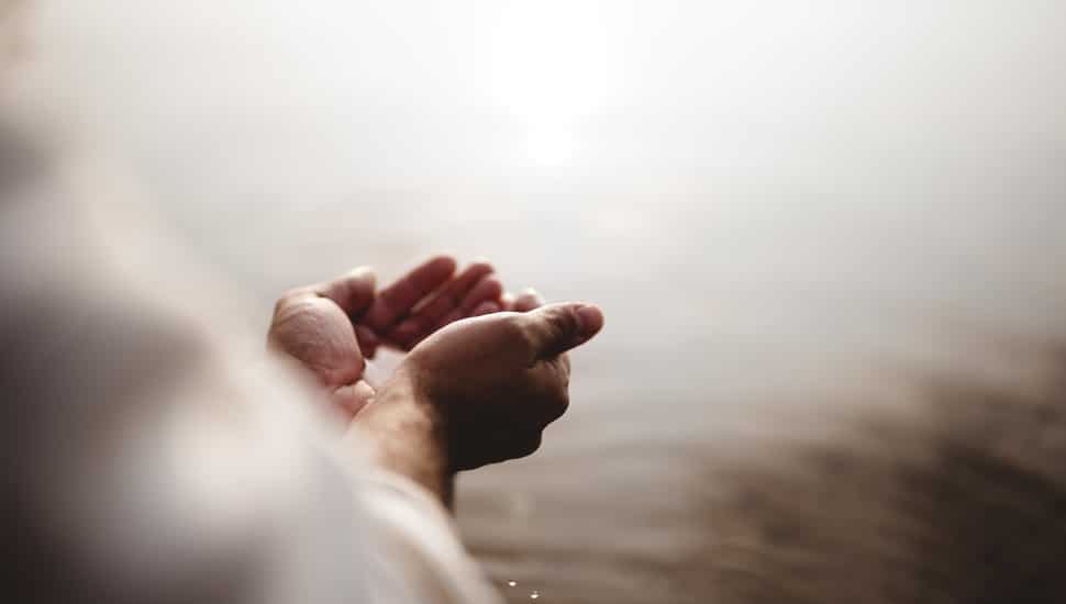 Close up image of hands scooping water, indicating baptism ceremony.