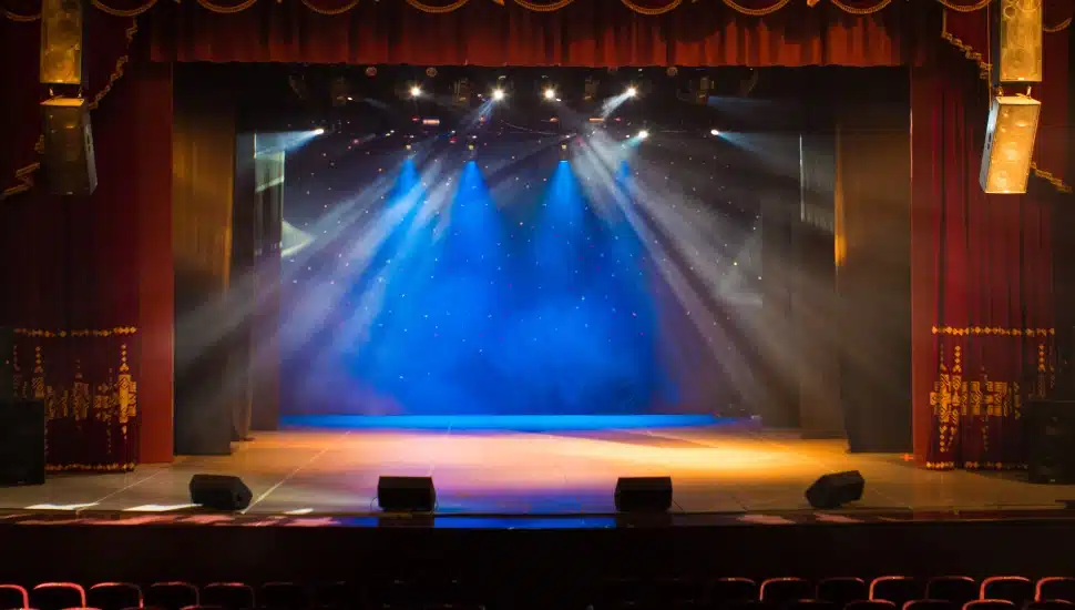 An empty stage of the theater, lit by spotlights and smoke.