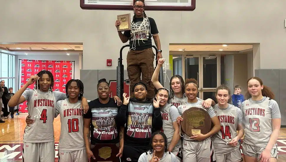 The Montgomery County Community College Mustangs women’s basketball team celebrates their historic victory after defeating Rowan College of South Jersey, Gloucester, 48-42 to win the North Atlantic District Championship—securing their first-ever Region Championship and a spot in the NJCAA Division III National Championship tournament. Group shot of the team holding trophy.