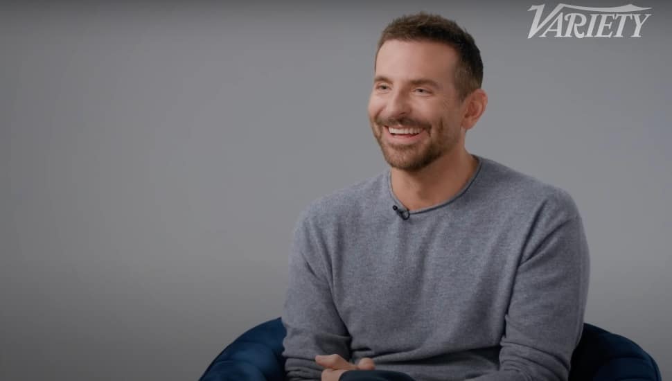 Bradley Cooper sitting and wearing a grey sweater.
