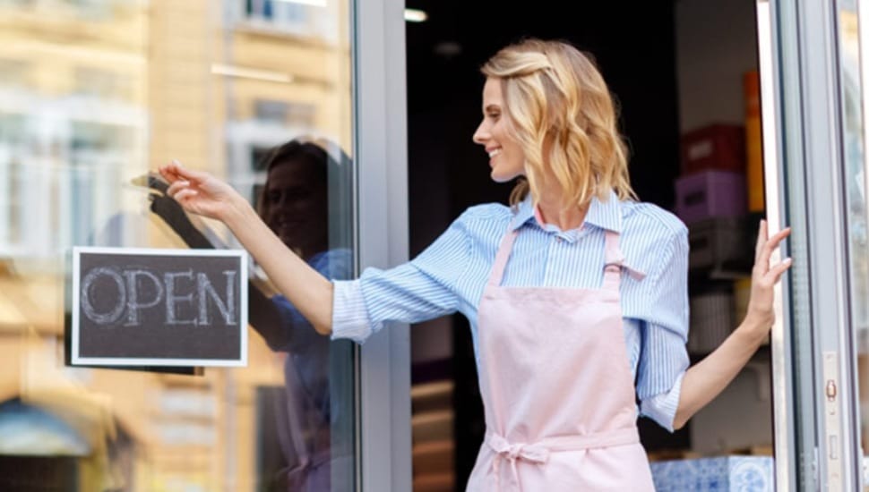 Woman business owner hangs open sign in window.