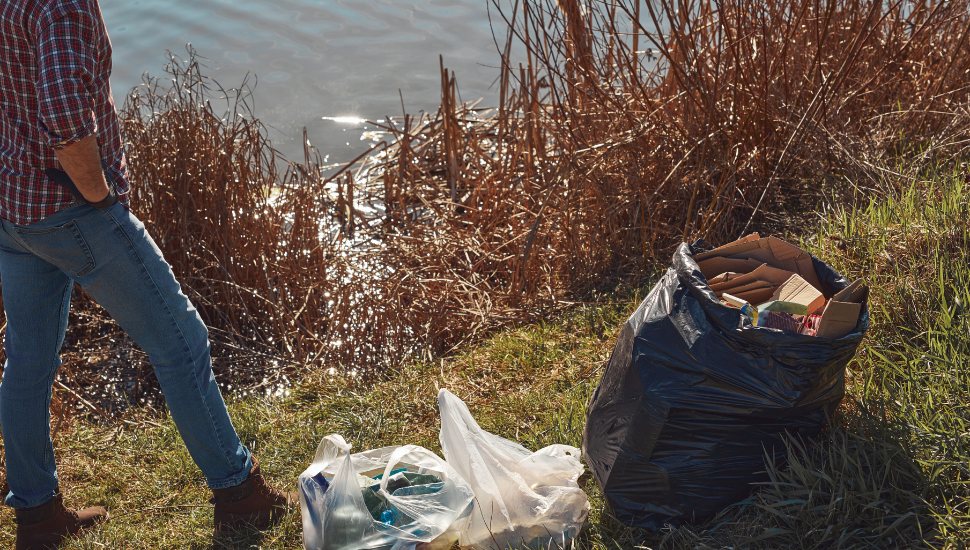 Volunteer and environmental activist cleaning dirty lake shore filled with trash.