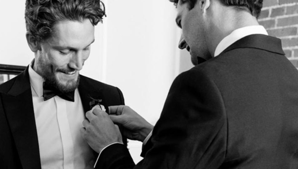 A man pins a corsage to another man's lapel.