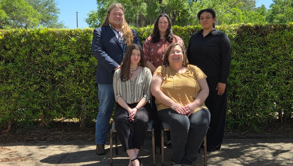 Five college students pose for group photo in front of bushes.