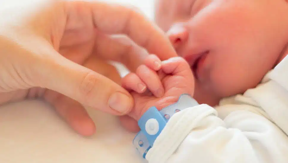 An infant gripping his mother's finger.