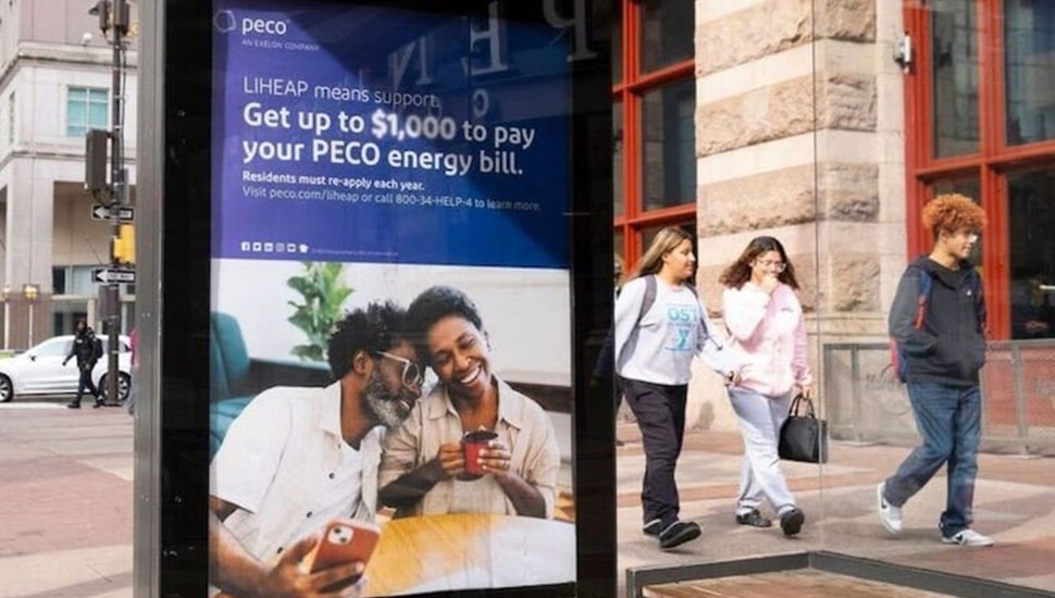 People walk past advertisement for utility bill financial relief.