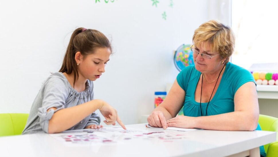 A woman therapist sitting at a table with a teenage girl as they work on a project together