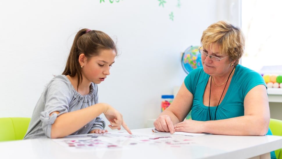 A woman therapist sitting at a table with a teenage girl as they work on a project together