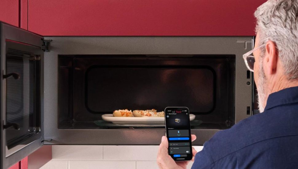 A man checks his kitchen app while opening his microwave.