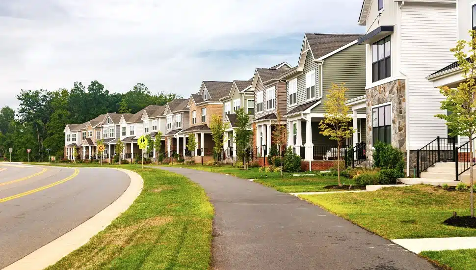 Quiet street in a residential area in the suburbs. Rows of houses along the sidewalk with a green lawn.