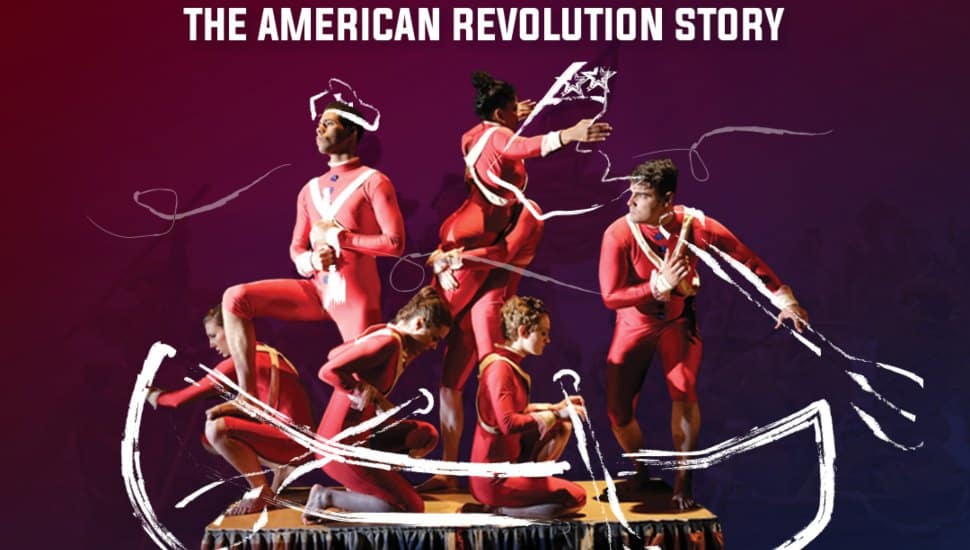 The image shows seven actors in vibrant, period-accurate costumes, standing together on a narrow, elevated platform. The actors are positioned in dynamic, action-filled poses that suggest movement and excitement, capturing the energy of the performance.