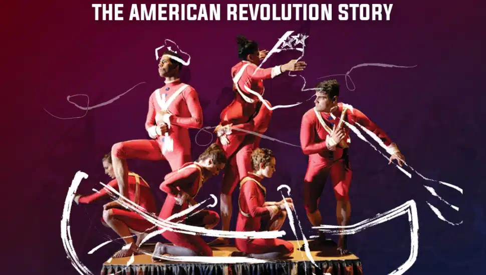 The image shows seven actors in vibrant, period-accurate costumes, standing together on a narrow, elevated platform. The actors are positioned in dynamic, action-filled poses that suggest movement and excitement, capturing the energy of the performance.