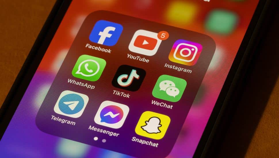 A smartphone displaying social media apps including TikTok, Facebook, Instagram, and Snapchat.