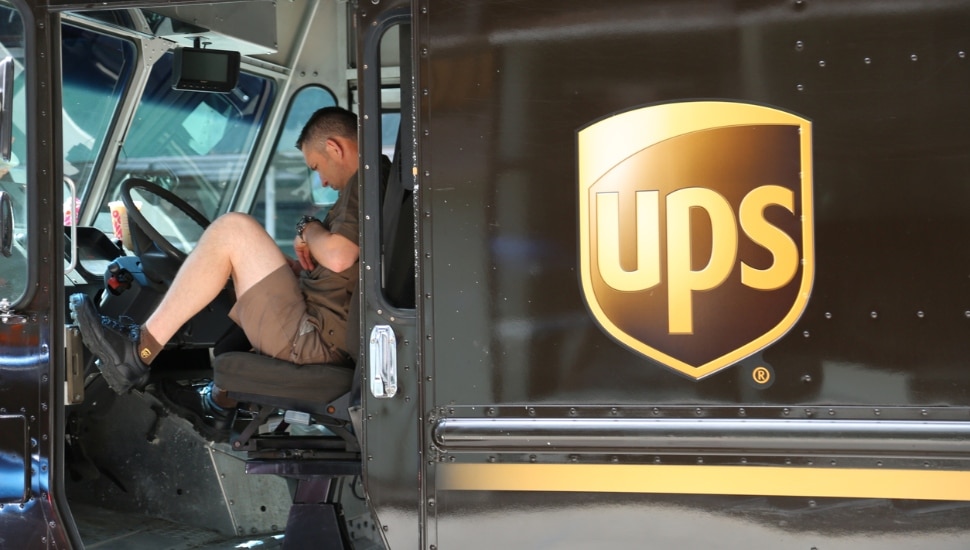 A UPS driver with a clipboard sitting inside a UPS truck.