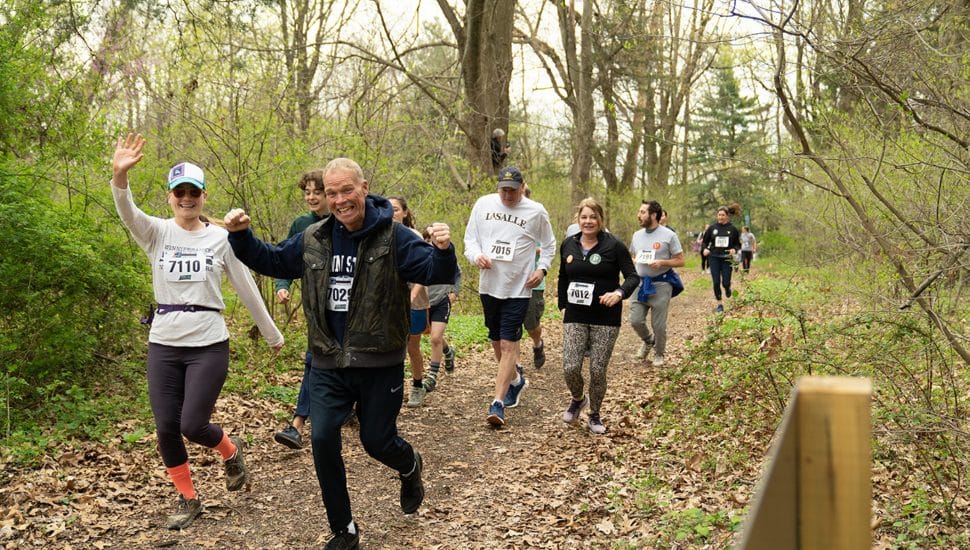 A group of happy runners waving at camera while running the Annual Trail Race hosted by Pennypack Ecological Restoration Trust.