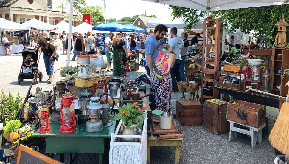 Shoppers browse vintage and handmade items at the outdoor Clover Market in Bryn Mawr, with colorful vendor tents, antique goods, and families enjoying a sunny spring day.