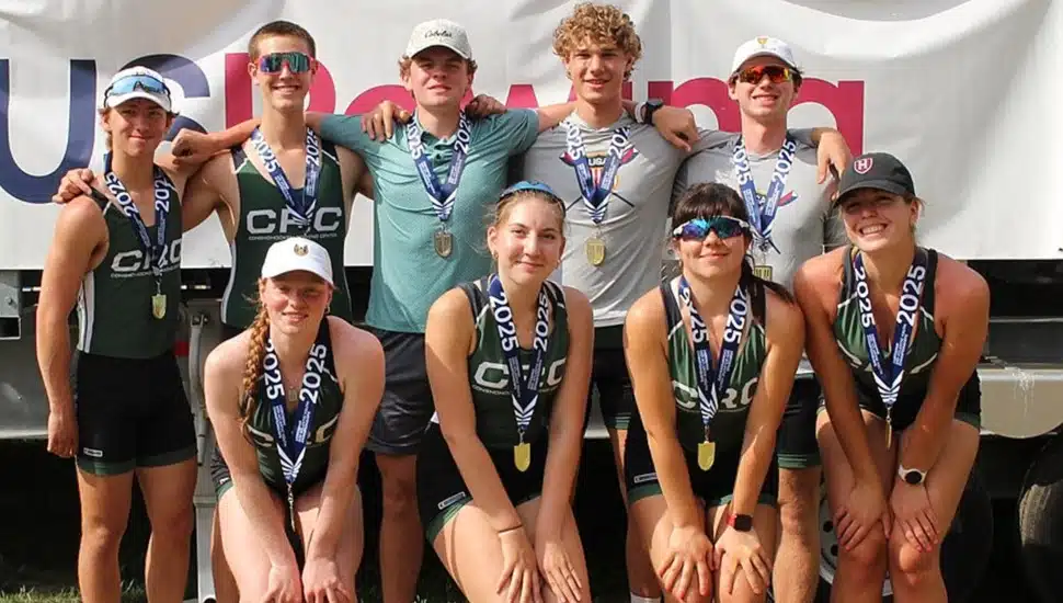 Teenage rowers in green jerseys and winning medals pose for a group photo.