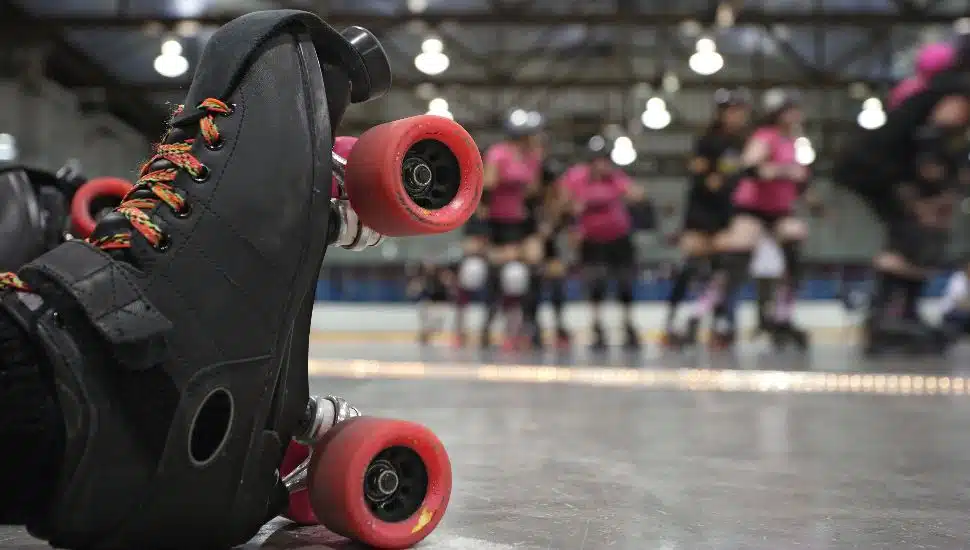 An abstract image of the roller-skates of a fallen skater as her teammates in the background continue to skate around the track of the roller derby.