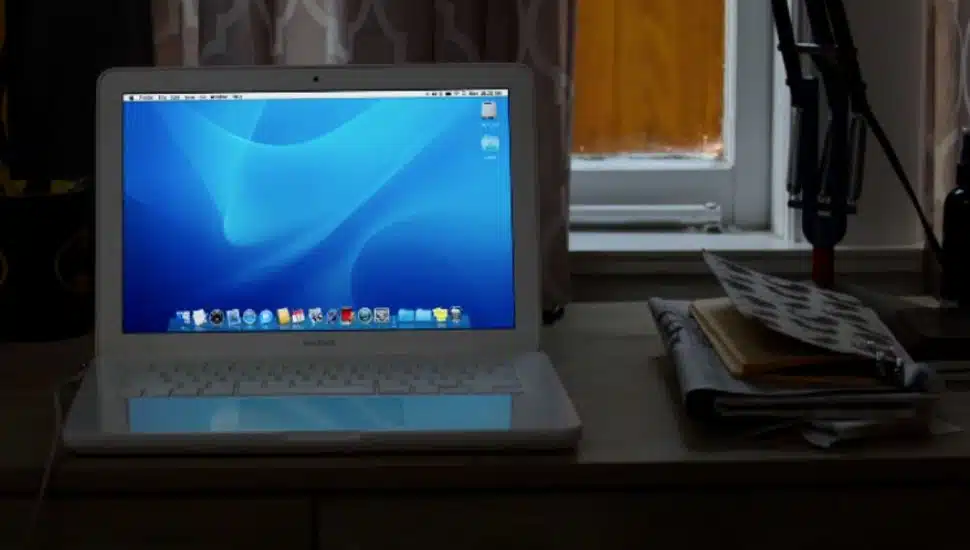 An older model MacBook laptop on a bedroom desk.