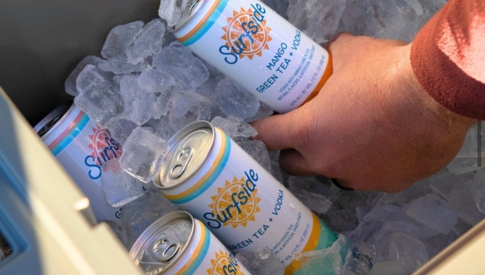 A hand grabbing a can of Surfside out of a cooler full of ice.