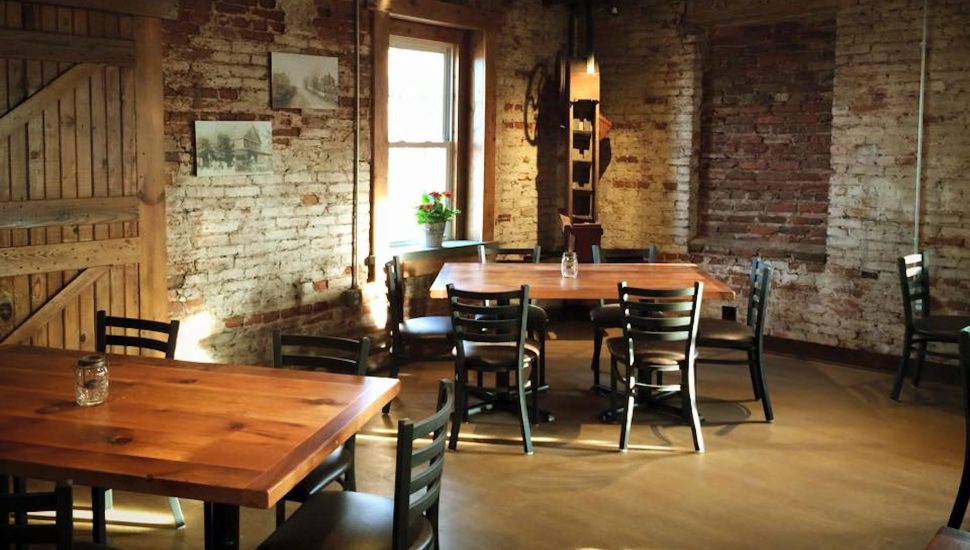An inside view of the seating area at The Mill. There are tables against a brick wall and there is a rustic aesthetic/soft lighting.