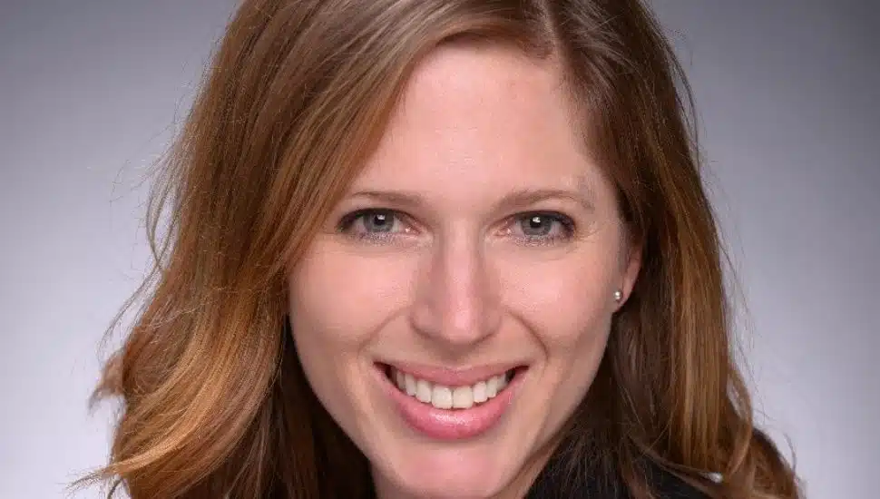 Headshot of Anna Brown: Light brown hair, smiling, against a grey-colored backdrop.