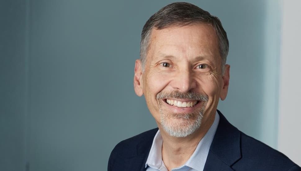 Headshot of older male business executive in dark suit jack and open collared shirt.