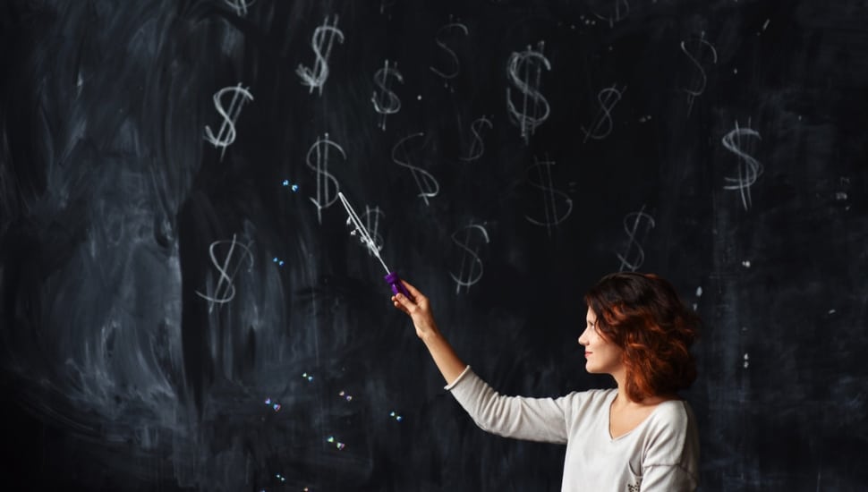 A teacher uses a pointer to point to dollar signs on a blackboard.
