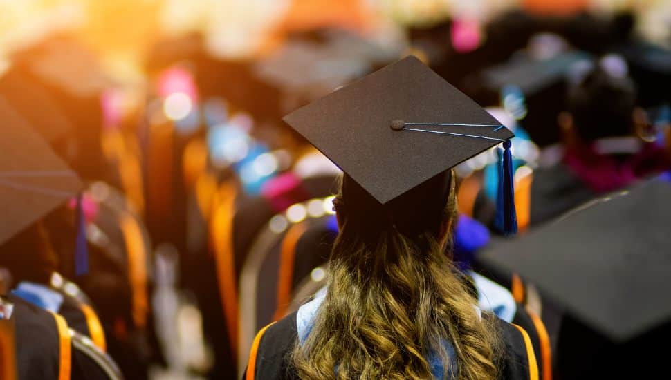 Rear view of a full class of graduates sitting, dressed in cap and gown, waiting to get degrees.
