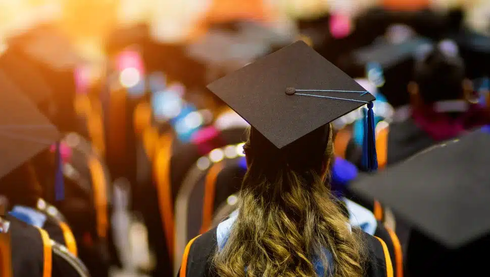 Rear view of a full class of graduates sitting, dressed in cap and gown, waiting to get degrees.